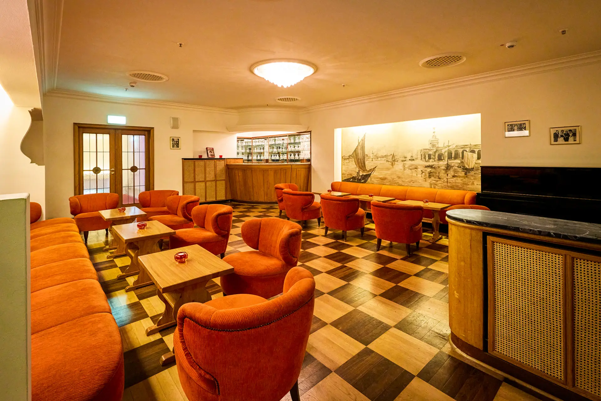 Im Bild ist das stilvolle Innere einer Lounge mit orangefarbenen Sesseln und gemustertem Holzboden.