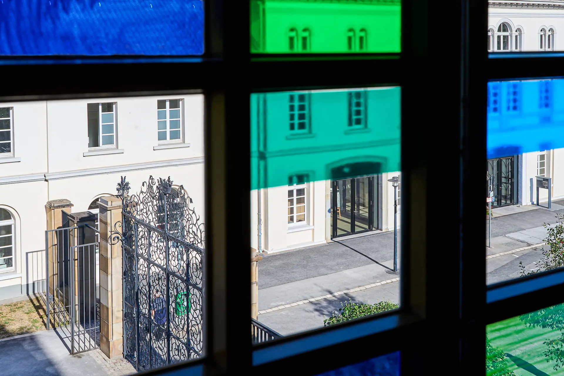 Blick durch bunte Fensterscheiben auf den Innenhof und das weiße Gebäude von Schloss Borbeck, Essen.