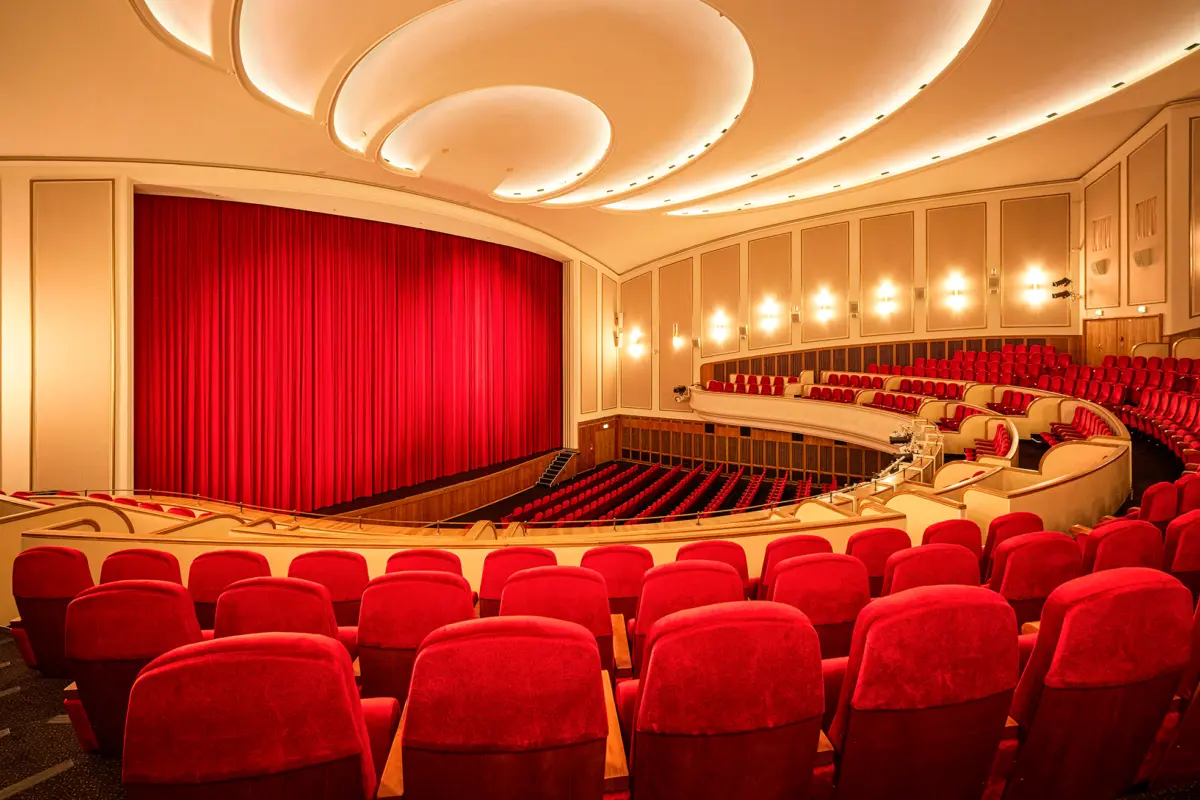 ```html Ein elegantes, leeres Theater mit roten Sitzen und geschlossenem, beleuchtetem Vorhang. ```