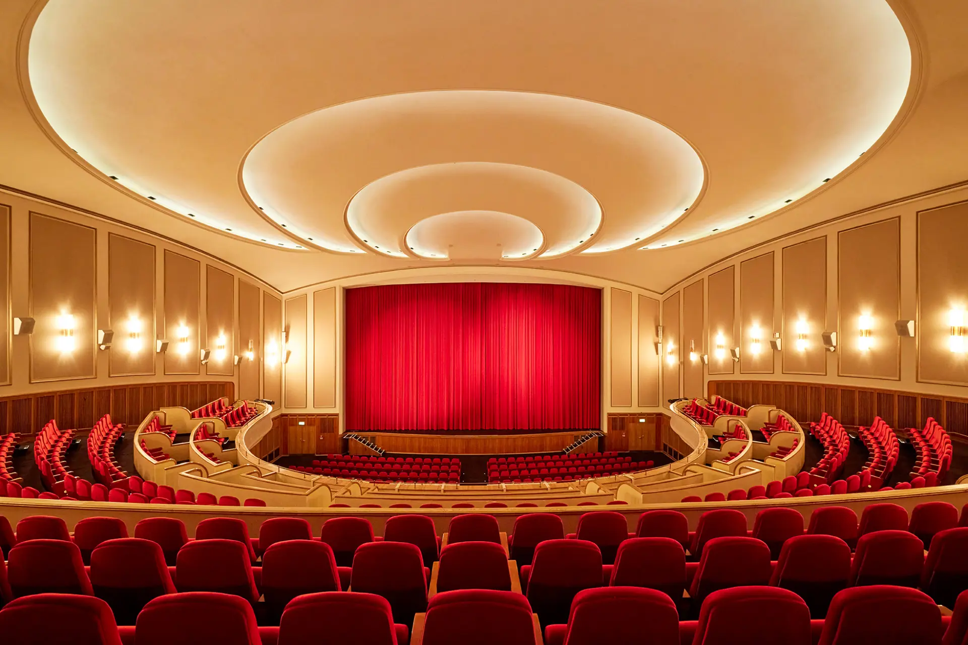 Das Bild zeigt ein klassisches Kino mit roten Samtsesseln und einer großen Leinwand im Zentrum.