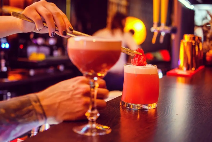 Zwei Cocktails auf einem Bartresen, eine Hand legt die Garnitur auf