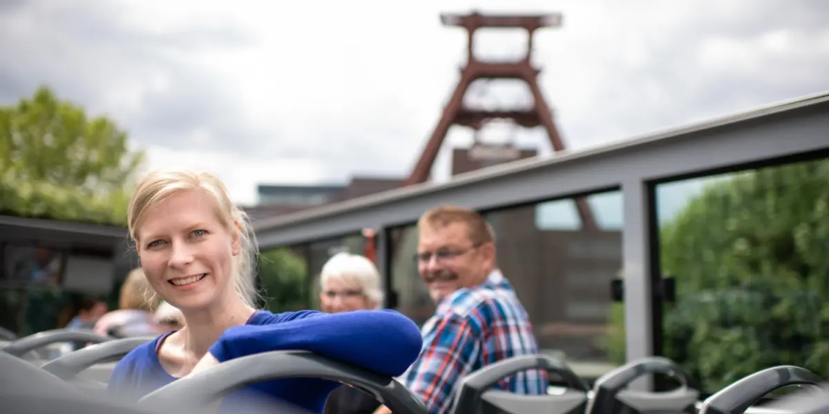 Fahrgäste im offenen Oberdeck des Cabriobusses vor dem Doppelbock von Zollverein