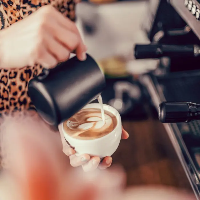 Barista gießt Milchschaum in eine Cappuccinotasse