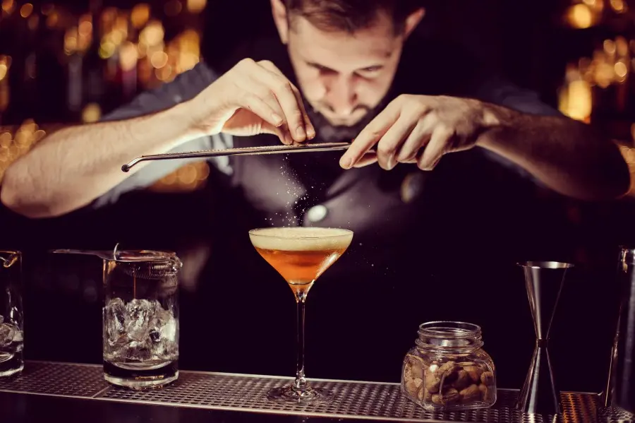 Barkeeper streut Gewürz über einen Cocktail auf dem Tresen