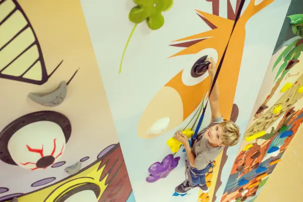 Kind klettert an einer bunt bemalten Boulderwand