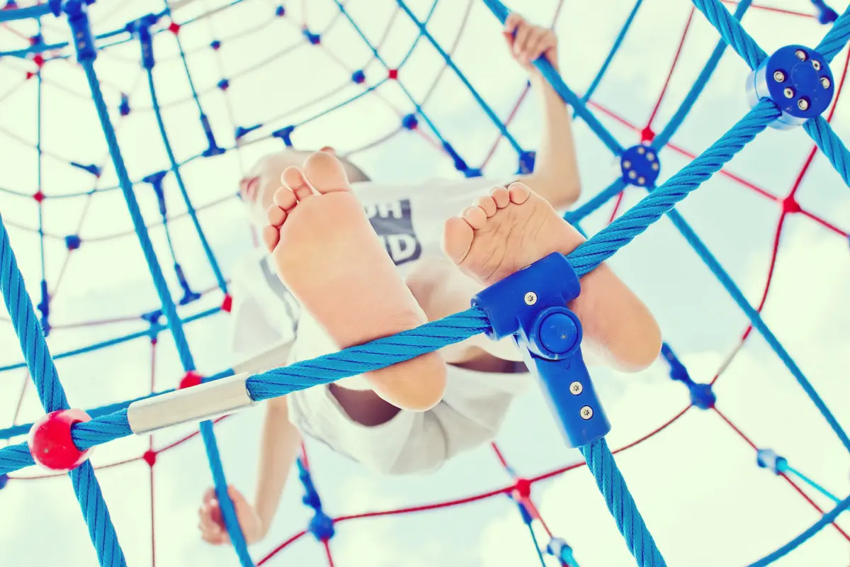 Kind in einem Kletternetz auf dem Spielplatz, von unten gesehen