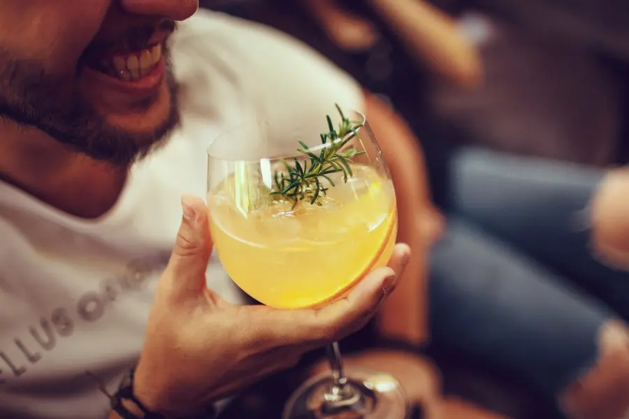 Lachender Mann hält ein Cocktailglas mit Rosmarinzweig