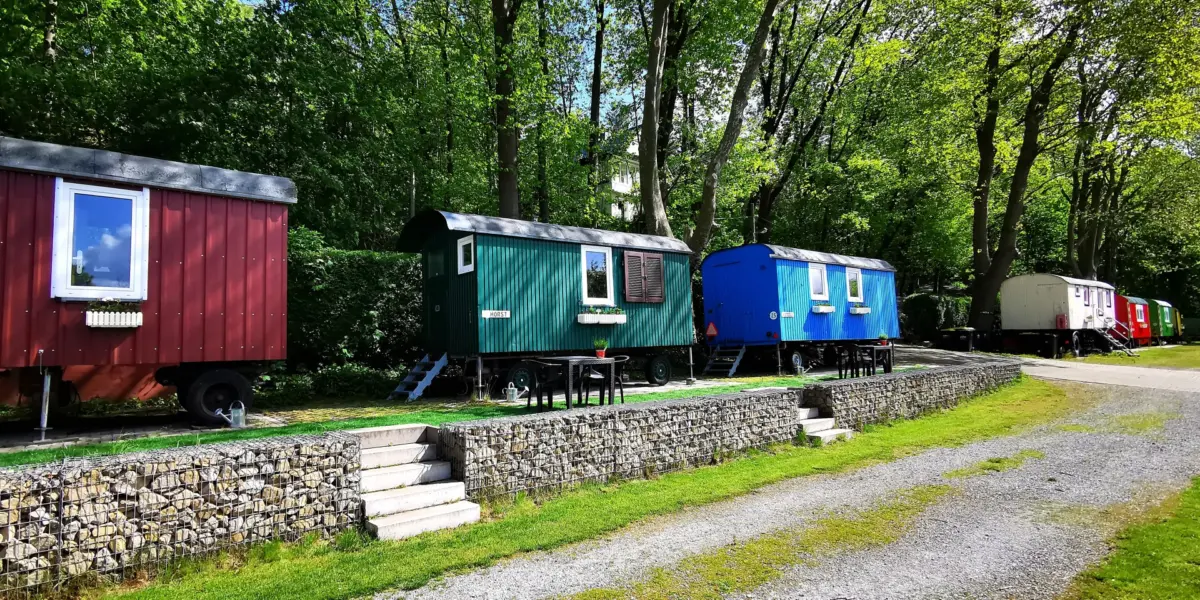 Bunte Bauwagen unter hohen Bäumen auf dem Ruhrcamping