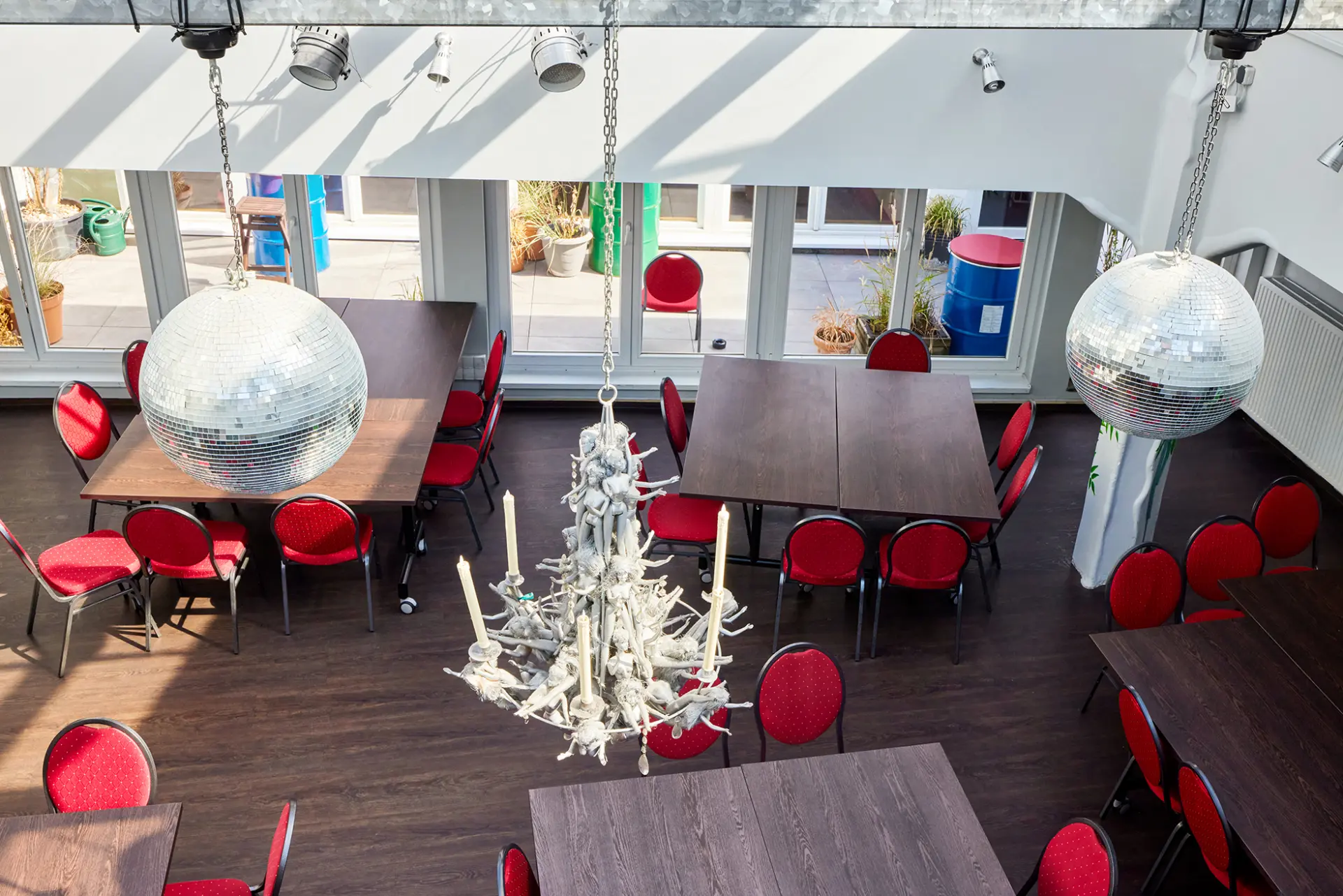 Großer, heller Raum mit roten Stühlen, Holztischen, Disco-Kugeln und Ast-Kronleuchter.