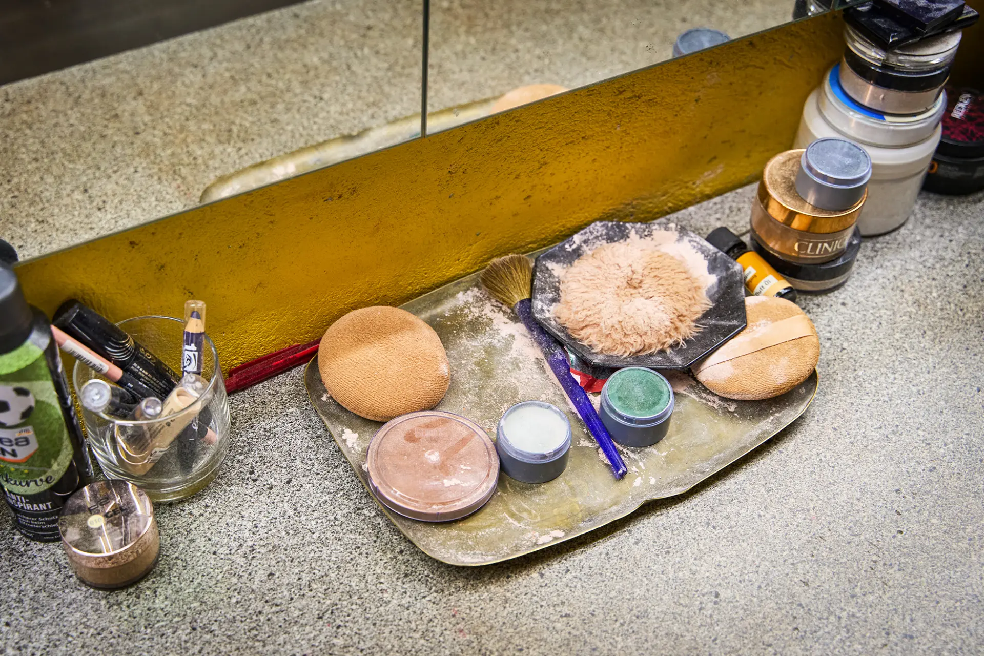 Schminkutensilien und Puder vor einem Spiegel auf einer Oberfläche arrangiert.