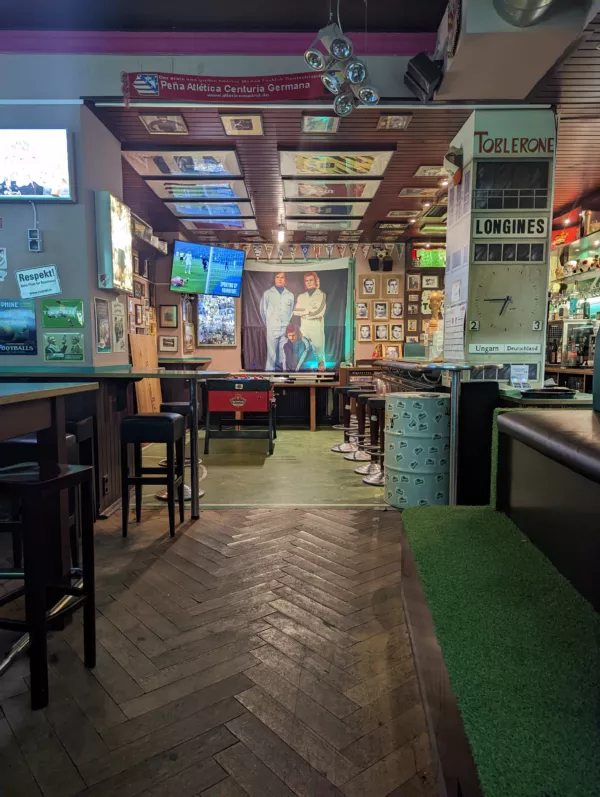 Gemütliche Bar mit Holzboden, vielen Fußballbildern an der Wand und Fernsehern, zeigt lebhafte Atmosphäre.