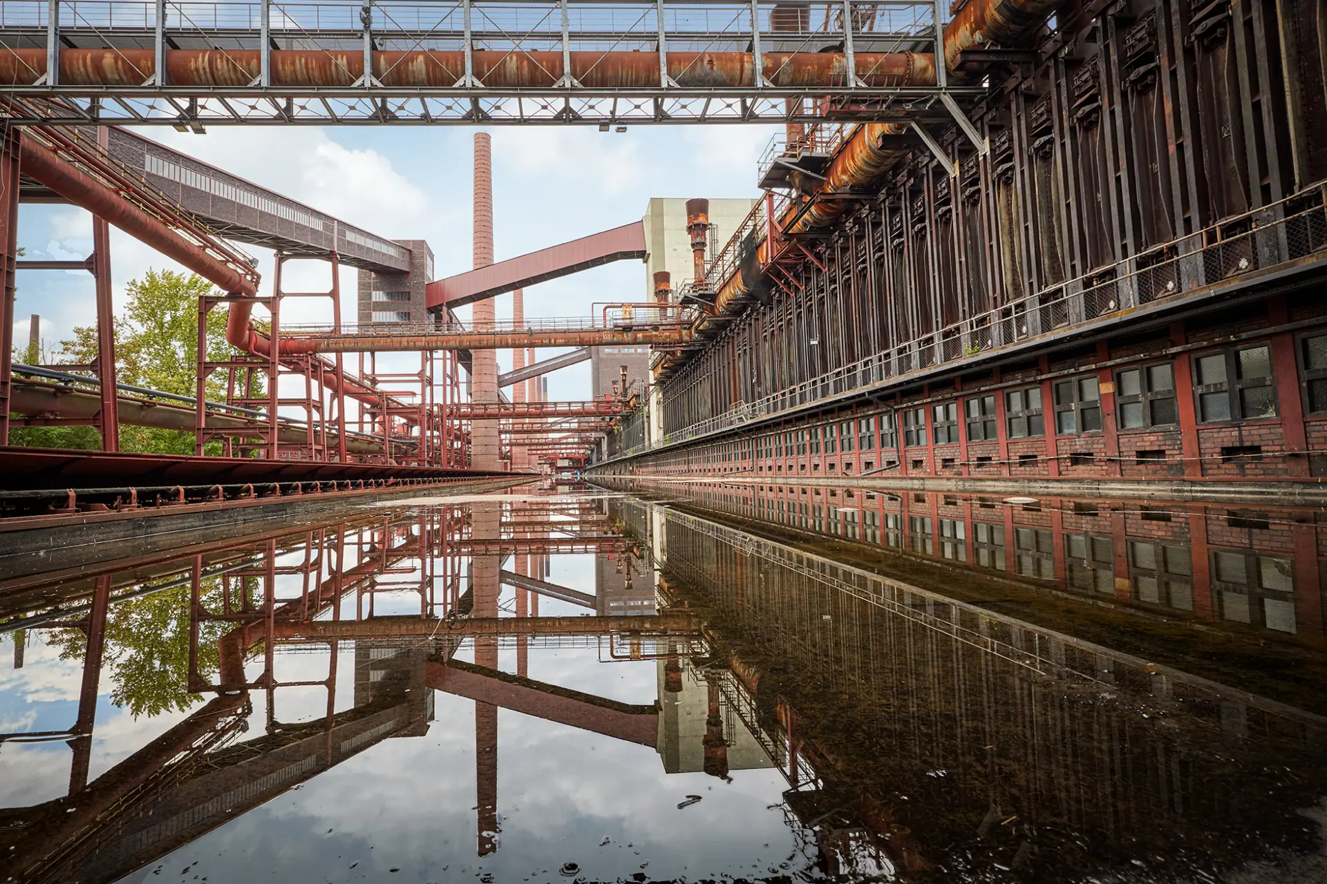 Industriekulisse mit vorhandenen Rohren und Strukturen, die sich in einer Wasserfläche spiegeln.