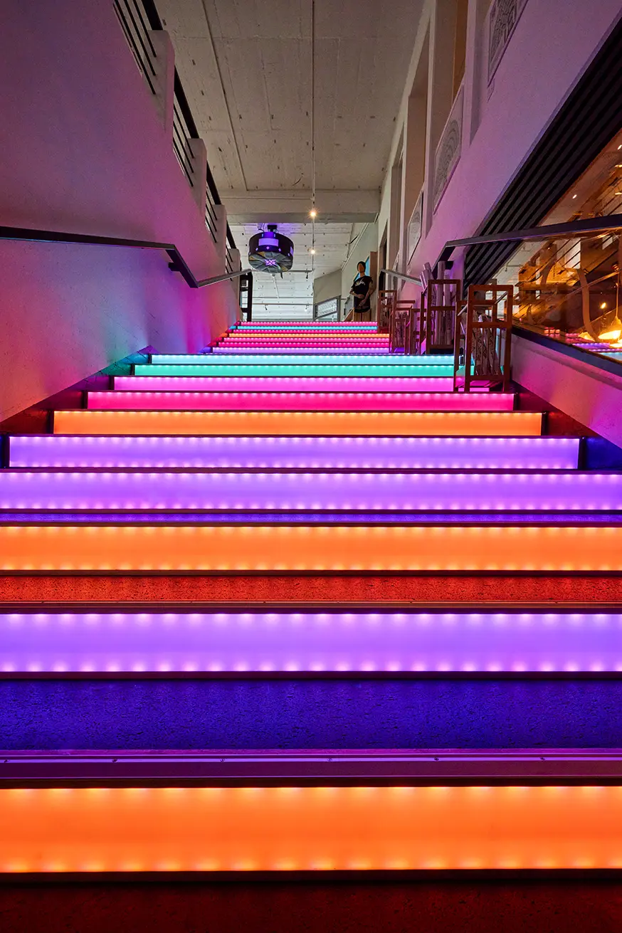 Bunte LED-beleuchtete Treppe im Unperfekthaus Essen, die in ein helles, modernes Obergeschoss führt.