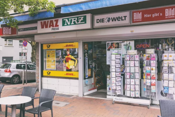 Shop-Fassade einer Zeitschriftenhandlung mit Zeitungsdrucken und Postdienst-Werbung.