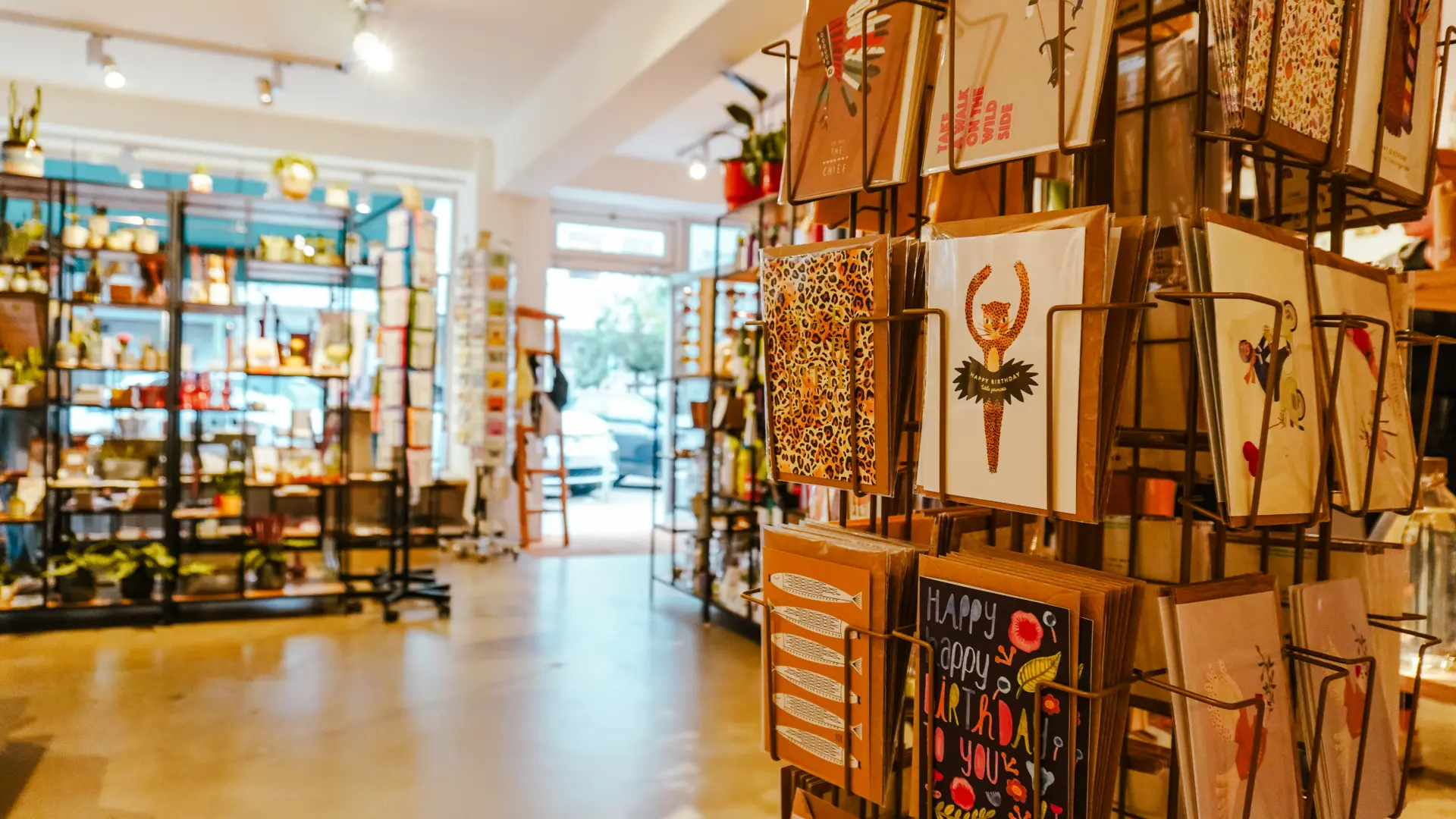 Alt-Text: Ein hell beleuchteter Geschenkeladen mit bunten Kartenständern und Regalen voller Produkte.