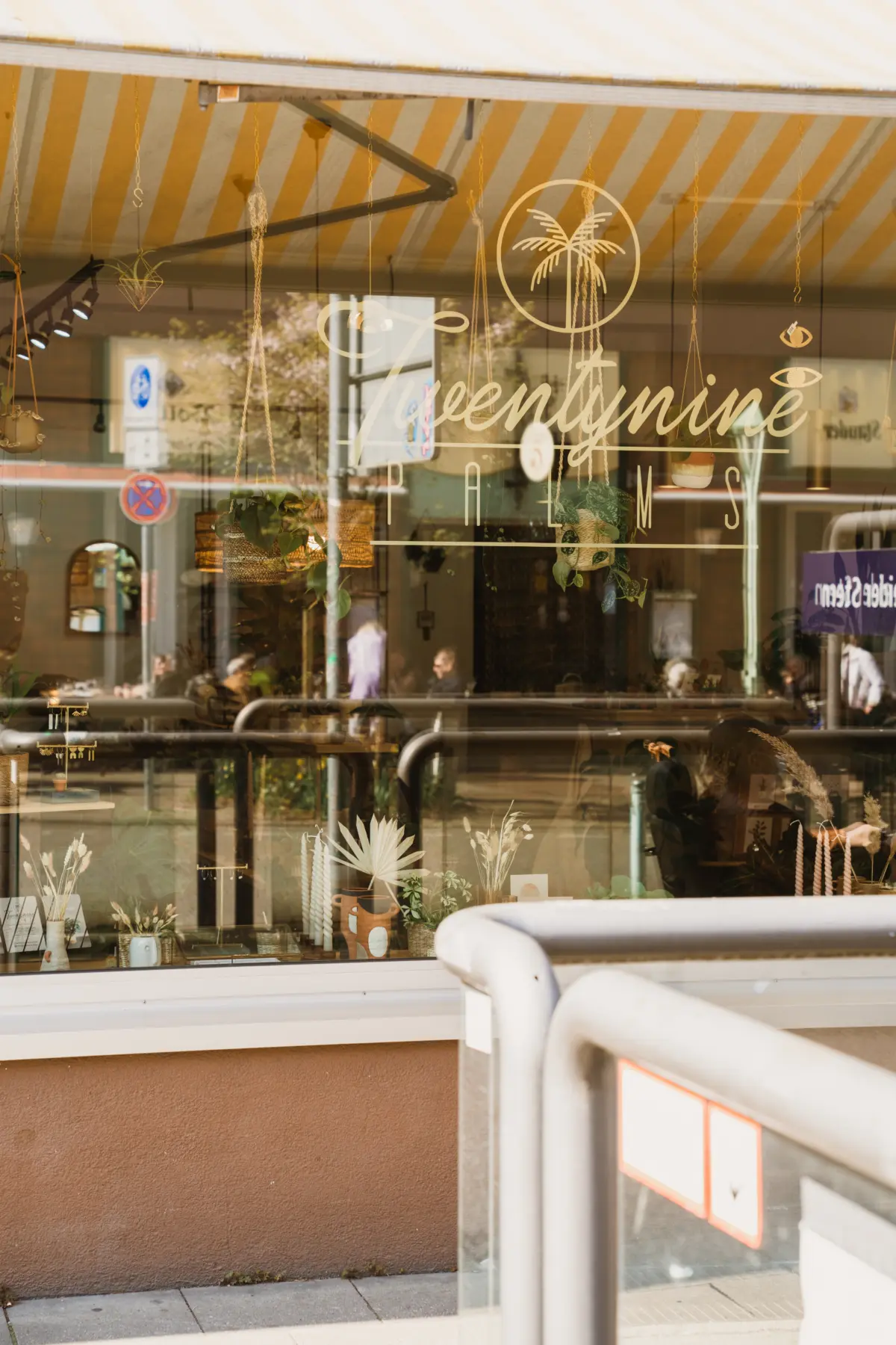 Schaufenster eines Cafés mit Schriftzug "Twentynine Palms", umgeben von Pflanzen und Dekoration.