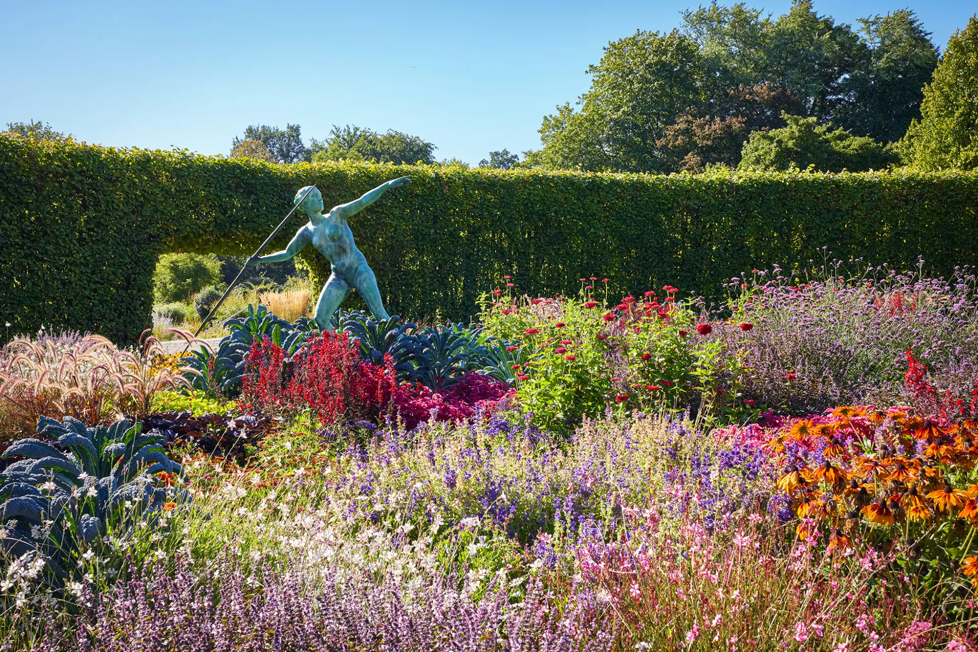 Eine bronzene Bogenschütze-Statue steht majestätisch inmitten eines farbenfrohen Blumenmeers im Garten.