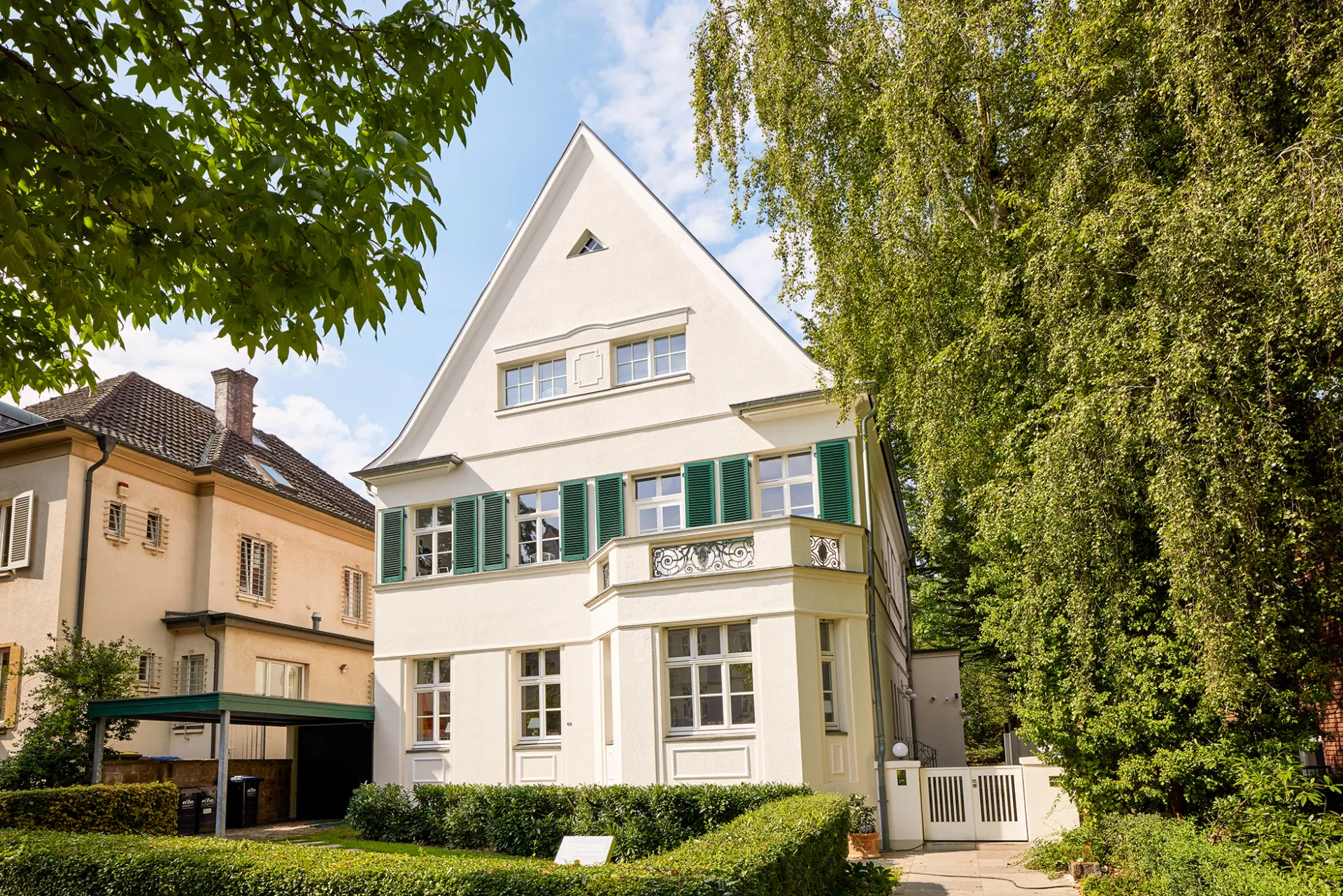Ein großes, weißes Wohnhaus mit grünen Fensterläden steht zwischen Bäumen im Moltkeviertel, Essen.