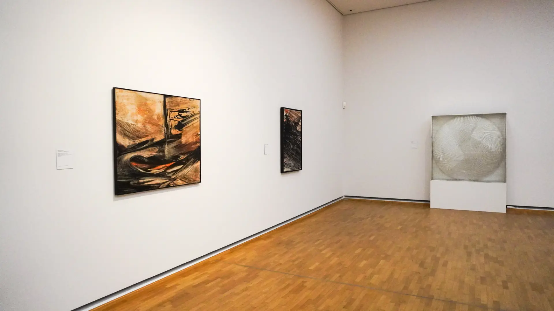 Das Bild zeigt einen modernen Galerieraum mit drei abstrakten Kunstwerken an den Wänden.
