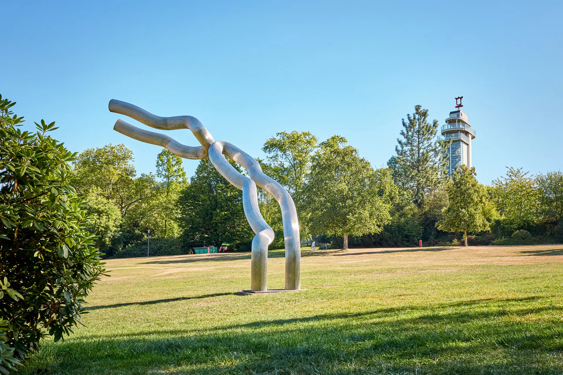 ```html Moderne Skulptur aus Metall auf grüner Wiese, im Hintergrund ein hoher Aussichtsturm. ```