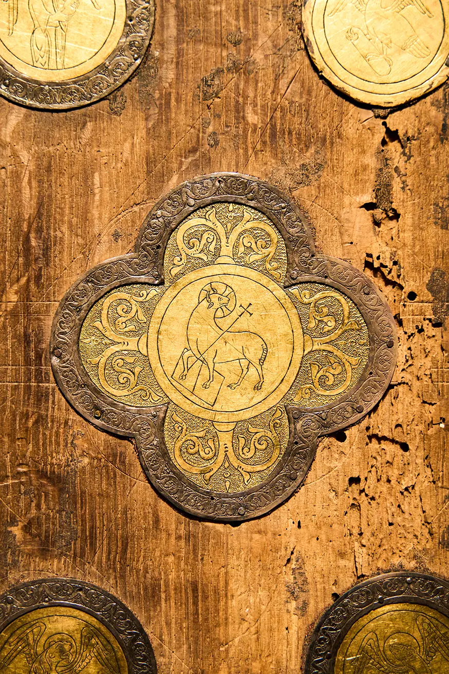 Ein kunstvoll geschnitztes Holzbrett mit goldenen, kreuzgeschmückten Lammverzierungen.