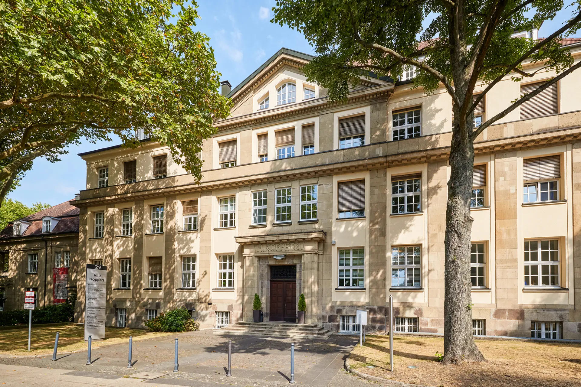 Historisches Gebäude mit hellem Putz und großen Fenstern, umgeben von üppigem Grün in Essen.