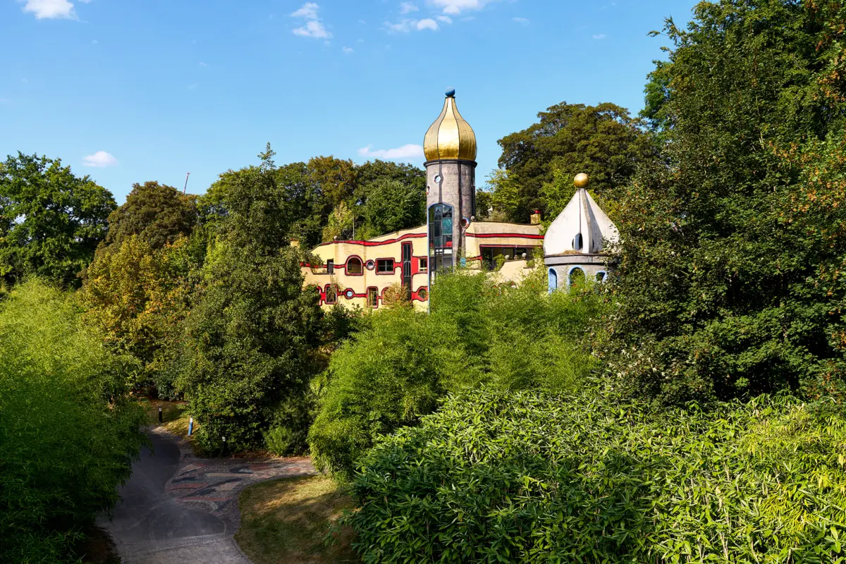 Das Bild zeigt ein farbenfrohes Haus mit goldener Kuppel, umgeben von üppigem Grün und Bäumen.