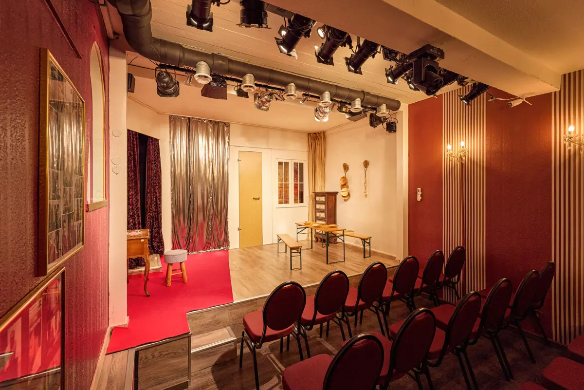 Gemütliches kleines Theater mit roten Stühlen und Bühne in intimer Atmosphäre.