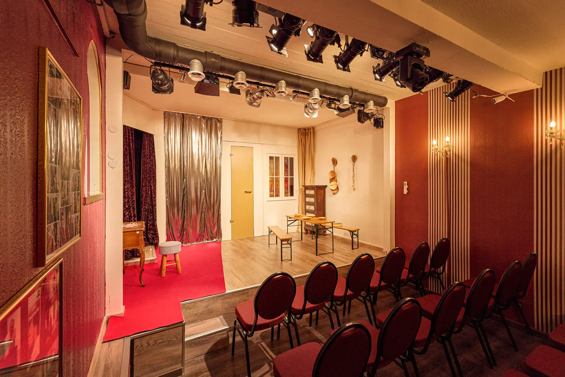 Gemütliches kleines Theater mit roten Stühlen und Bühne in intimer Atmosphäre.