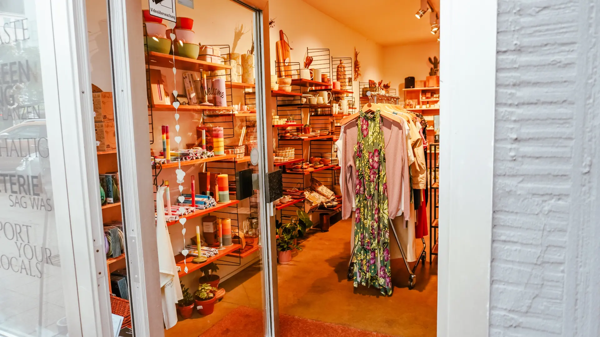 Blick in einen einladenden Laden, bunt dekoriert mit Kleidung, Pflanzen und Alltagsgegenständen.
