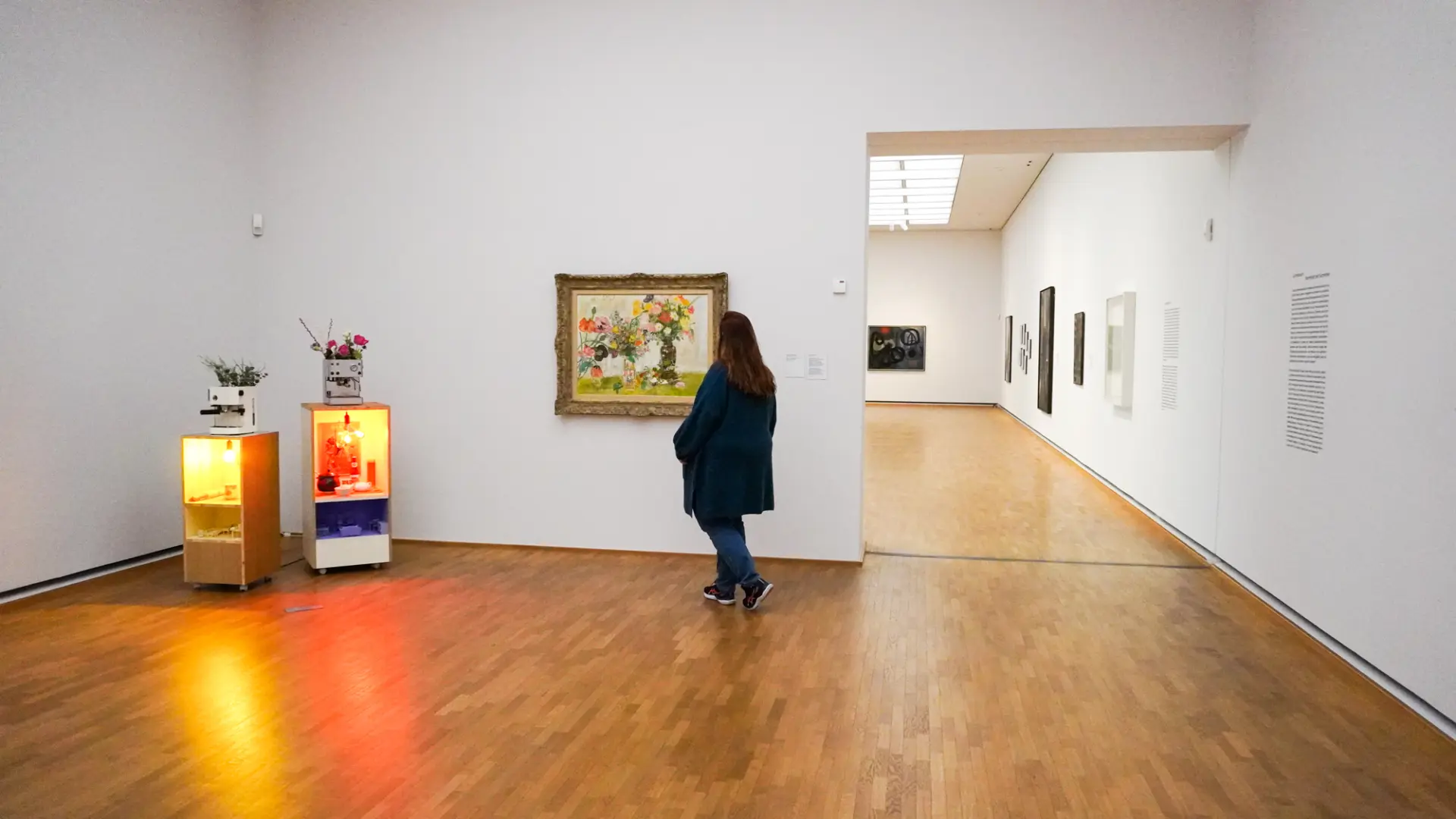 Eine Person betrachtet Kunst in einem modernen, minimalistischen Galerieraum mit Holzfußboden.