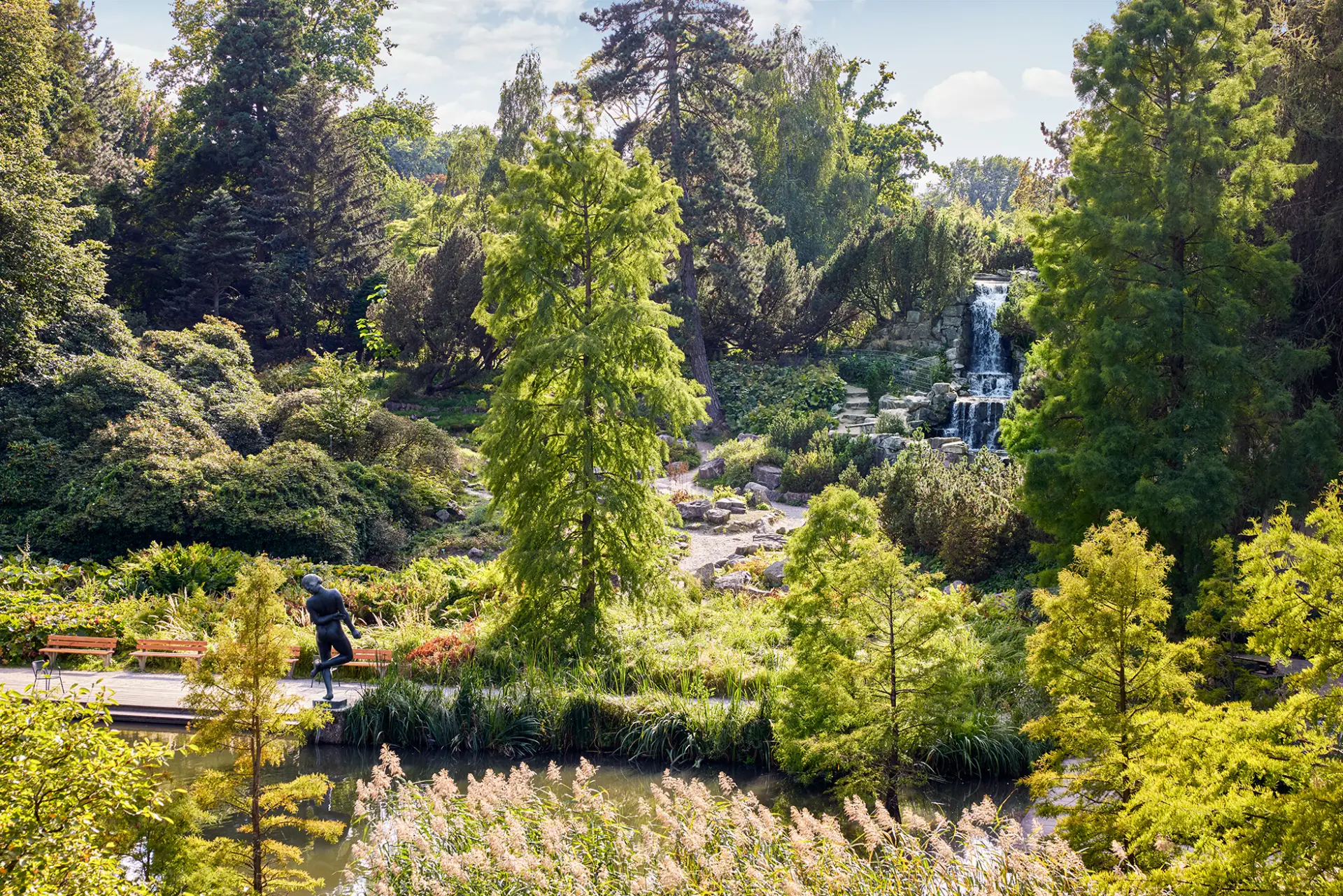 Grüne Parklandschaft mit Wasserfall und Spaziergänger auf einem Weg in Essen.