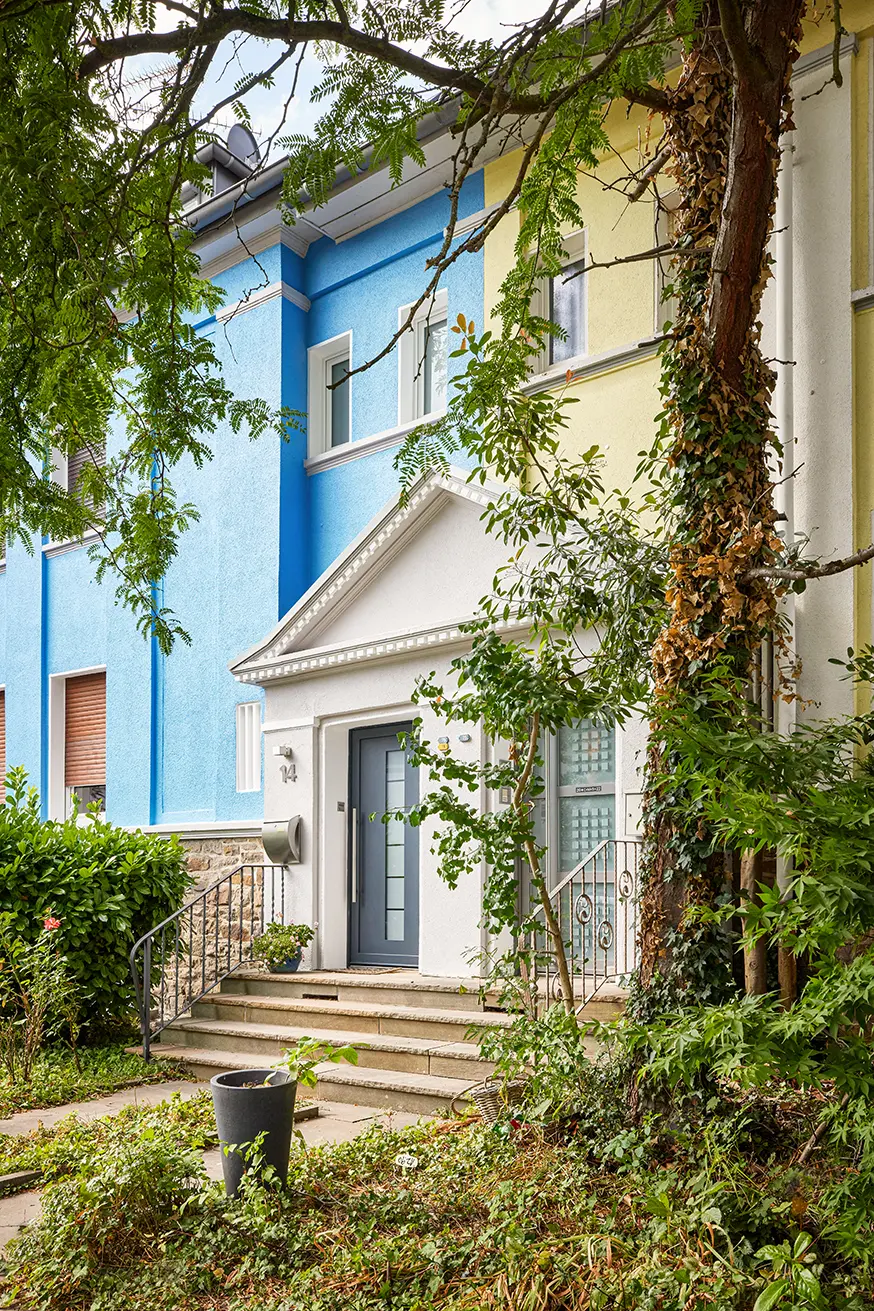 Mehrfarbiges Haus in Essen mit blauen und gelben Fassaden, begrüntem Eingang und Details.
