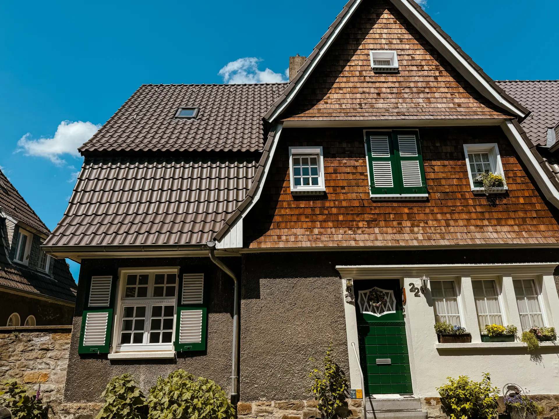 Ein traditionelles Fachwerkhaus mit grünem Türrahmen, Holzschindeln und blauem Himmel im Hintergrund.