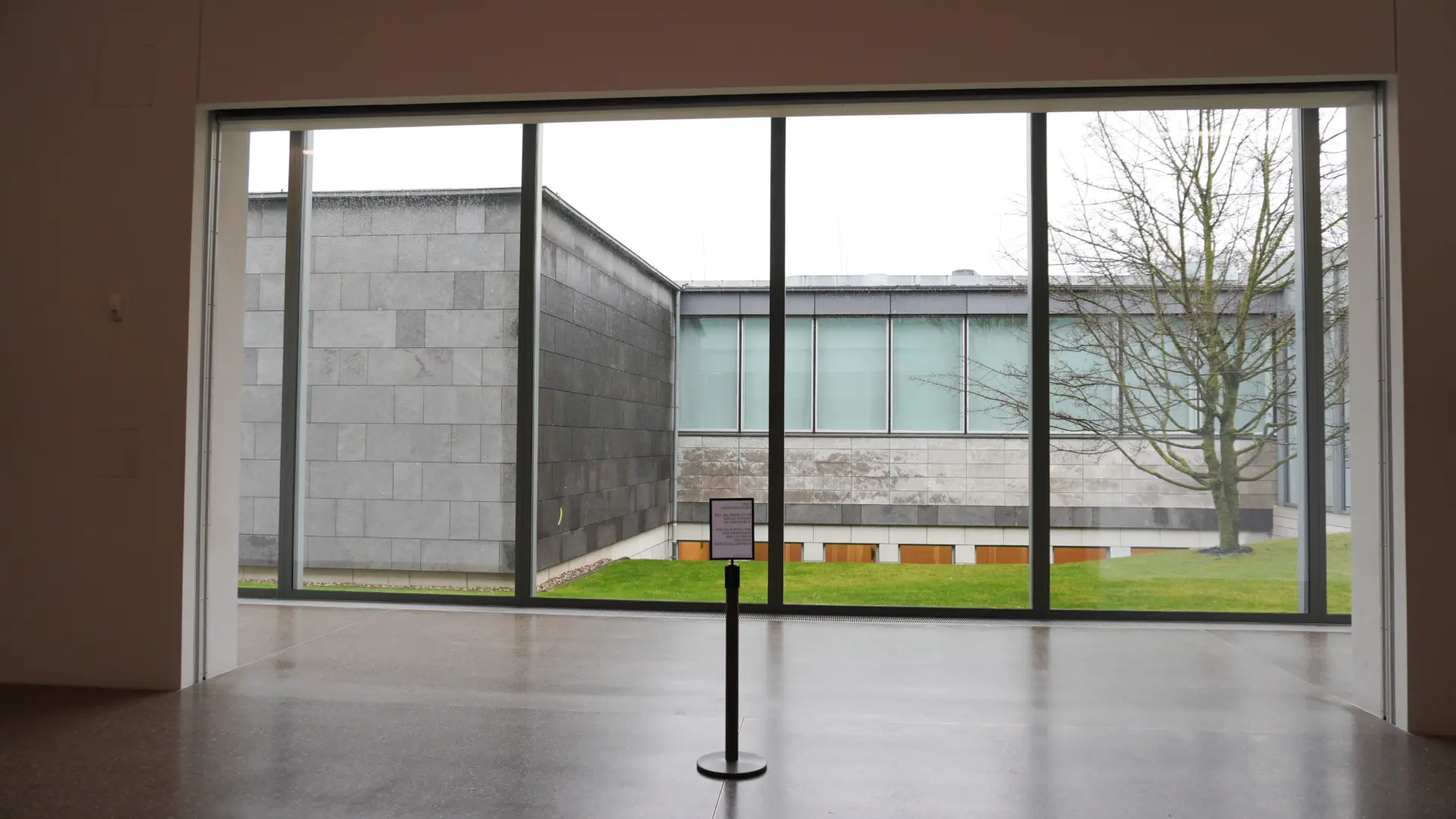 Blick aus einem modernen Museumsfenster auf minimalistisches Außendesign mit Glasfronten und Beton.