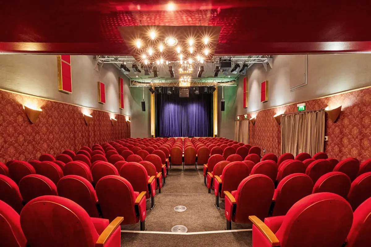 Innenansicht eines Theaters in Essen mit roten Samtsitzen und einem beleuchteten Bühnenvorhang.