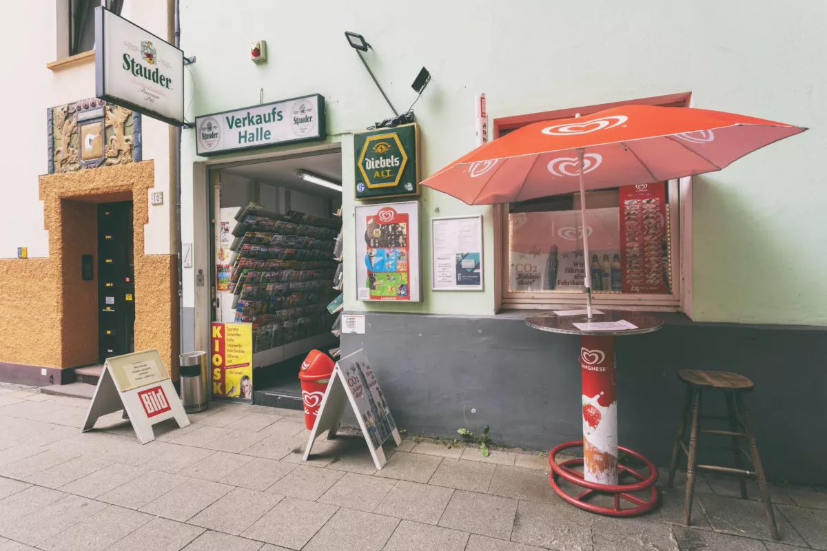 Verkaufsstand mit rotem Eisschirm und Produkten. Außenbereich mit Automaten und Werbeschildern.