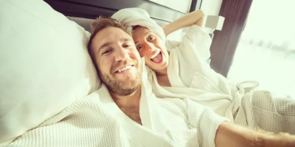 Paar im Bademantel macht ein Selfie im Hotelbett