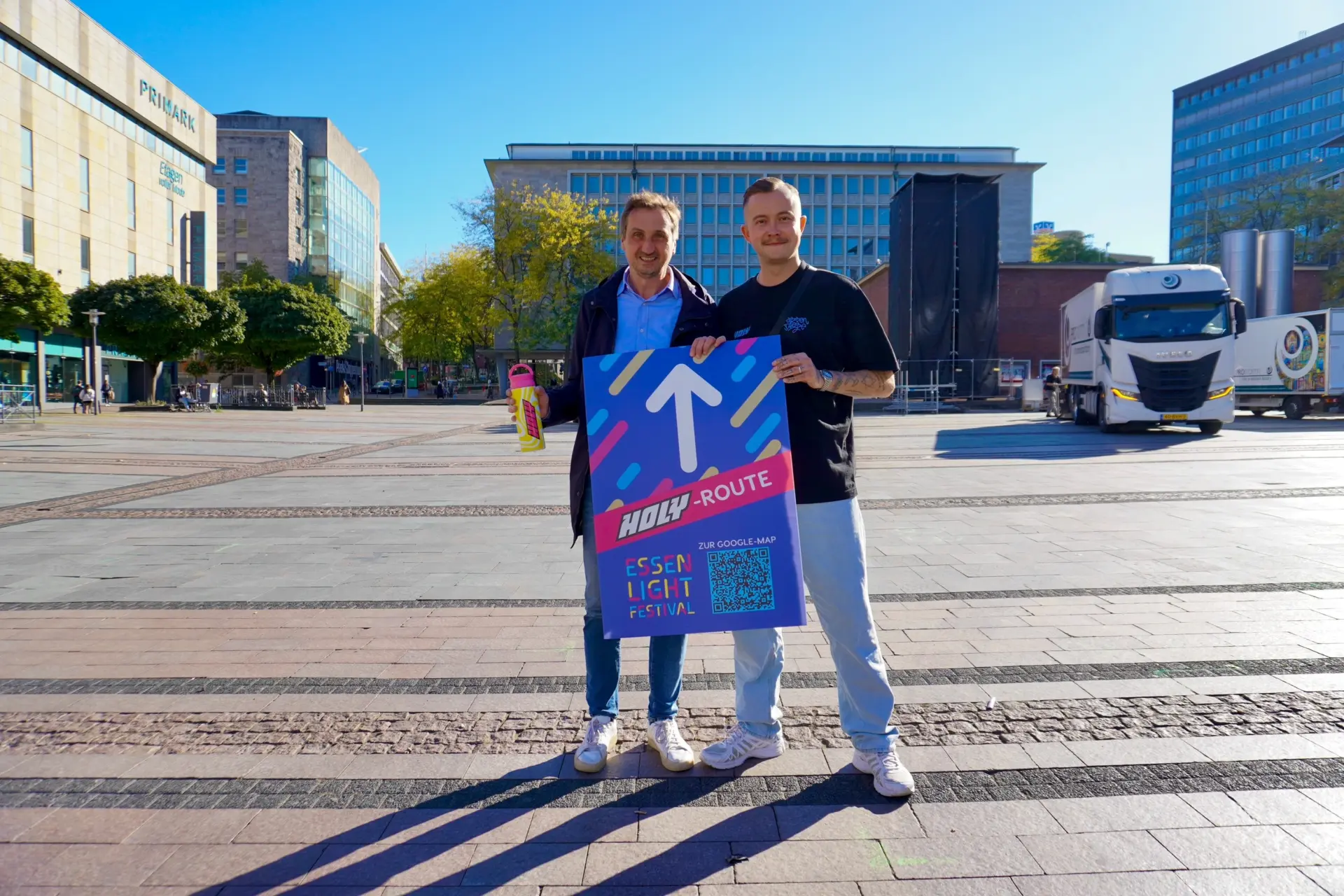 Carsten Hinzer, Brand Activation Lead bei HOLY und EMG-Geschäftsführer Richard Röhrhoff präsentieren auf dem Kennedyplatz die neue Routenbeschilderung des Festi